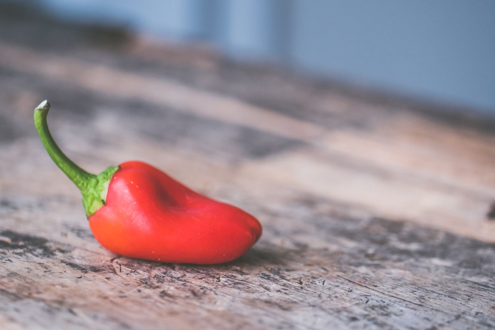 A vivid close-up of a fresh red chili pepper resting on a rustic wooden table.